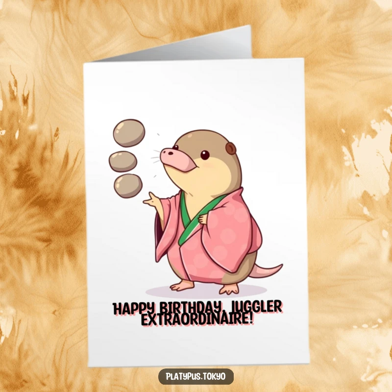 Funny Free Printable Birthday Card featuring a platypus in a vibrant kimono playfully juggling three smooth, round pebbles with a cheeky grin.